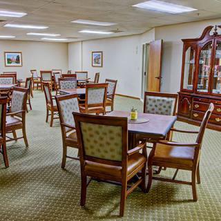A spacious dining room featuring multiple tables and chairs, with a carpeted floor and a display cabinet.