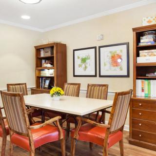 A cozy dining room with a wooden table, chairs, bookshelves, and framed artwork on the wall.