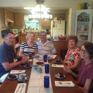 A group of people sitting around a dining table ready for a meal in a kitchen setting.