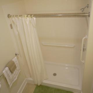 A bathroom with a shower and white curtain, featuring a grab bar for safety.