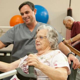 A nurse assists an elderly woman during a physical therapy session.