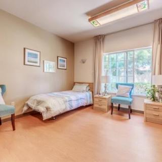 A cozy bedroom with a single bed, armchair, and large window.