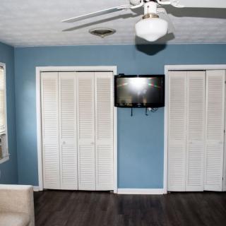 A bedroom with blue walls, featuring a ceiling fan, two closet doors, and a mounted television.