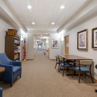 A well-lit hallway featuring seating, a table with chairs, a bookshelf, and artwork on the walls.