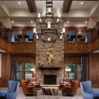 A beautifully designed living room featuring a stone fireplace, wooden beams, and elegant furniture under a grand chandelier.