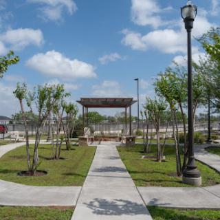 A serene park featuring well-maintained pathways, lush greenery, and a pavilion under a bright blue sky.