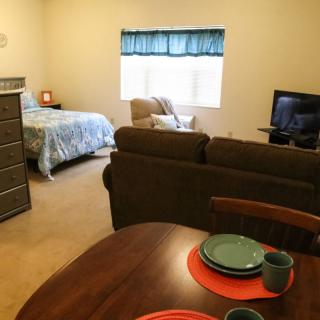 A cozy studio apartment featuring a bed, living area with a TV, and a small dining setup.