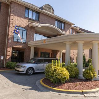 A hotel entrance with a car parked outside, featuring columns and a flag.