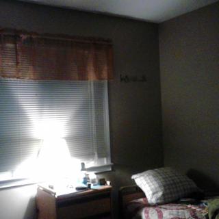 A small bedroom with sunlight streaming through a window, illuminating a bed and lamp.