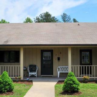 A cozy single-story house with a front porch, seating, and small trees lining the walkway.