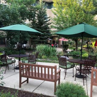 A peaceful garden patio with tables, chairs, and umbrellas surrounded by lush greenery.