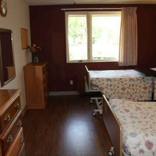 A cozy nursing home room with two beds and wooden furniture.