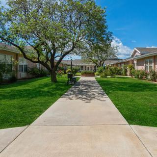 A scenic view of a pathway leading through a landscaped area with trees and buildings under a clear blue sky.