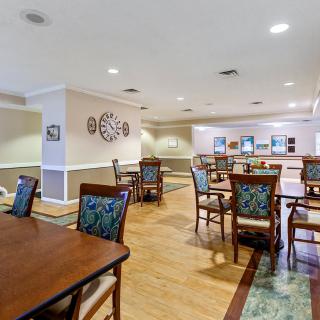 A spacious dining area with multiple tables and chairs, featuring a decorative wall clock and wooden flooring.