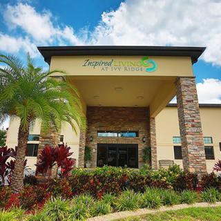 Front view of a well-landscaped building entrance with a palm tree and cloudy sky.