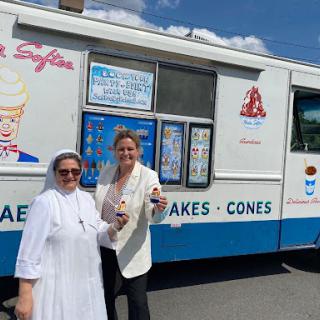 Two women enjoying ice cream outside an ice cream truck on a sunny day.
