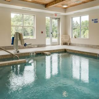 An indoor swimming pool with bright natural light streaming through the windows, featuring a pool lift for accessibility.
