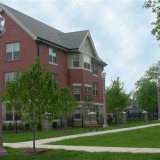 A brick residential building surrounded by a green lawn with trees and a sidewalk.