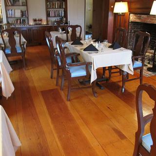 A cozy dining area with neatly arranged tables and chairs, featuring a fireplace and wooden floors.