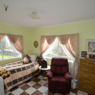 A cozy bedroom featuring a bed, recliner, and natural light from large windows.
