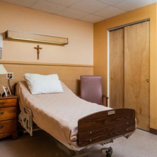 A hospital room with a single bed, bedside table, and a cross on the wall.