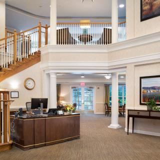 The image shows a spacious lobby area with a reception desk, staircase, and elegant decor.