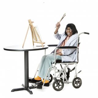 A person in a wheelchair enthusiastically holding a paintbrush near an easel.