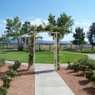 A serene outdoor garden featuring a beautifully crafted archway leading to a gazebo, surrounded by lush greenery under a clear blue sky.