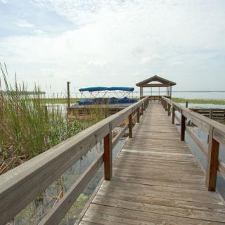 A wooden dock leading to a boat on a calm lake under a cloudy sky.