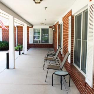 A covered porch with chairs against a brick wall and large windows.