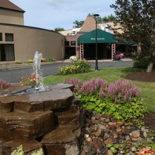 A landscaped entrance featuring a small fountain and green awning.