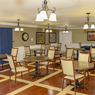 A well-lit dining room with several tables and chairs, featuring decorative paintings on the walls and a wooden floor.