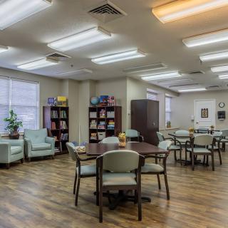 A cozy and well-lit lounge area with tables, chairs, bookshelves, and comfortable seating.