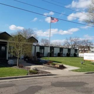 A building with an American flag on a flagpole, surrounded by trees and a neatly maintained lawn under a partly cloudy sky.
