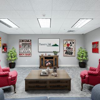 A modern office seating area with red chairs, artwork on the walls, and decorative plants.