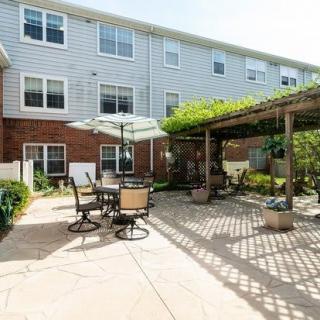 A cozy outdoor patio area with seating and a pergola, adjacent to a multi-story building.