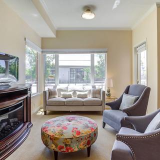 A cozy living room with a sofa, armchairs, a floral ottoman, and large windows providing natural light.