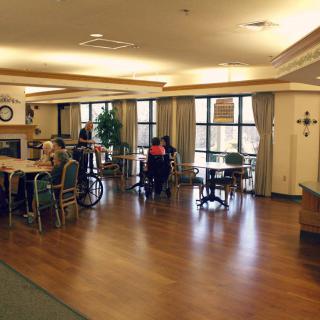 A cozy nursing home common area with residents seated at tables.