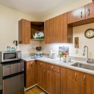 A compact modern kitchen with wooden cabinets, featuring a microwave and sink.
