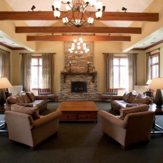 A cozy living room with a fireplace and elegant chandelier, featuring comfortable seating and wooden beam accents.