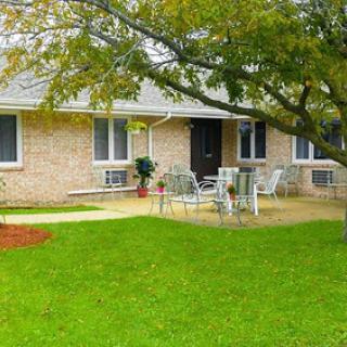 A charming house with a well-kept lawn and patio area, surrounded by trees.