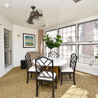 A bright sunroom with a dining table, surrounded by large windows and decorated with indoor plants.