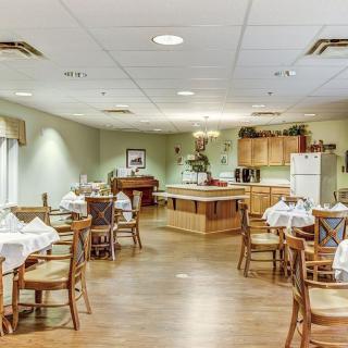 A spacious dining room with neatly arranged tables and chairs, adjacent to a kitchen area.