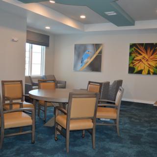 A dining room with a round table, several chairs, and artwork on the walls.