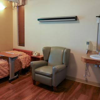 A hospital room with a bed, chair, and sink.