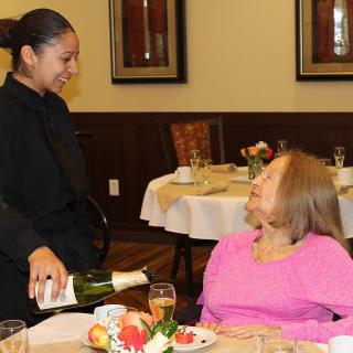 A server pours wine for a customer seated at a dining table.