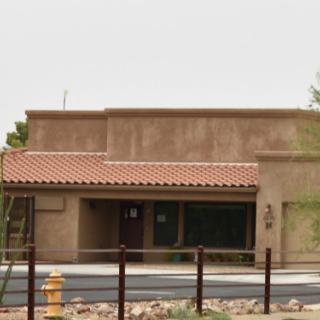A desert adobe-style building with a tiled roof and surrounding fence.