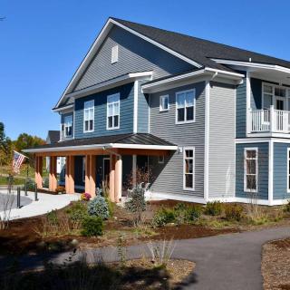 A modern residential house with blue siding and white trim, surrounded by a landscaped yard.