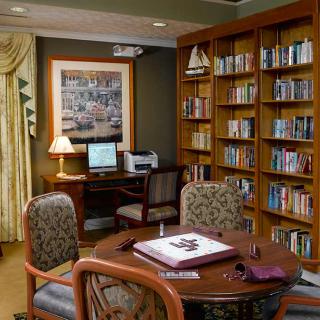 A cozy library setting with bookshelves, a computer, and a round table with chairs.
