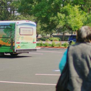 A person walking in a parking lot towards a parked bus with trees in the background.